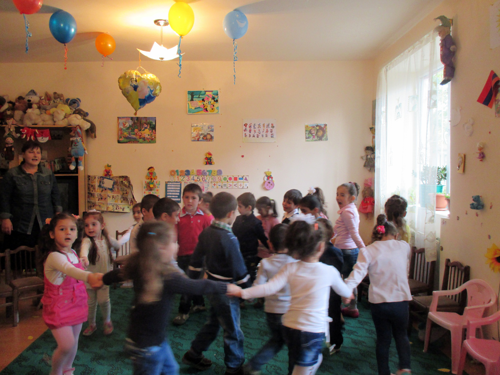 Viele Kinder tanzen im Kreis im geschmückten Kindergartenraum in Alaverdi